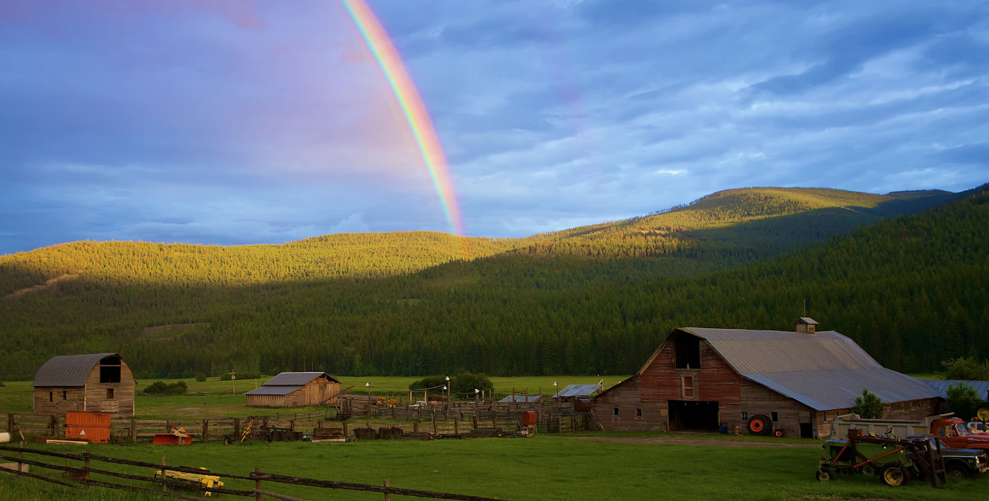A wooden barn and green field beneath a rainbow in eastern Idaho