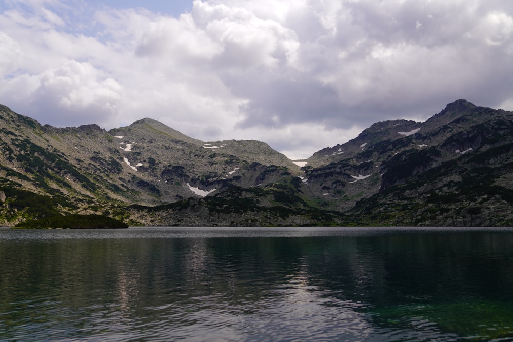 lake near mountain under cloudy sky during daytime