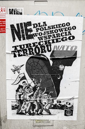 A poster with bold text in Polish related to political or military issues, featuring a black and white illustration of a large animal, possibly a bull, with human figures and a vehicle or military aircraft. The figures are depicted with expressive gestures, suggesting a theme of protest or opposition.