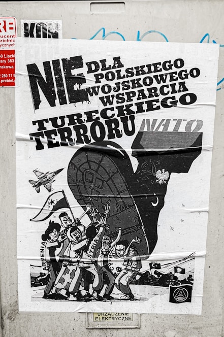 A poster with bold text in Polish related to political or military issues, featuring a black and white illustration of a large animal, possibly a bull, with human figures and a vehicle or military aircraft. The figures are depicted with expressive gestures, suggesting a theme of protest or opposition.