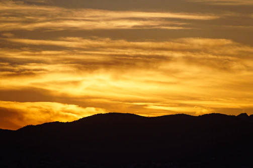 A vibrant sunset over a rugged mountain range captured from a camper van window.