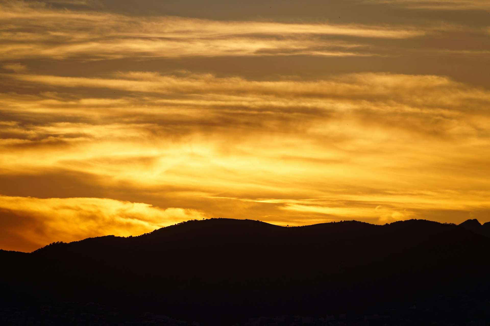 A vibrant sunset over a mountain range, with rich golden hues lighting up the sky and silhouetting the peaks.