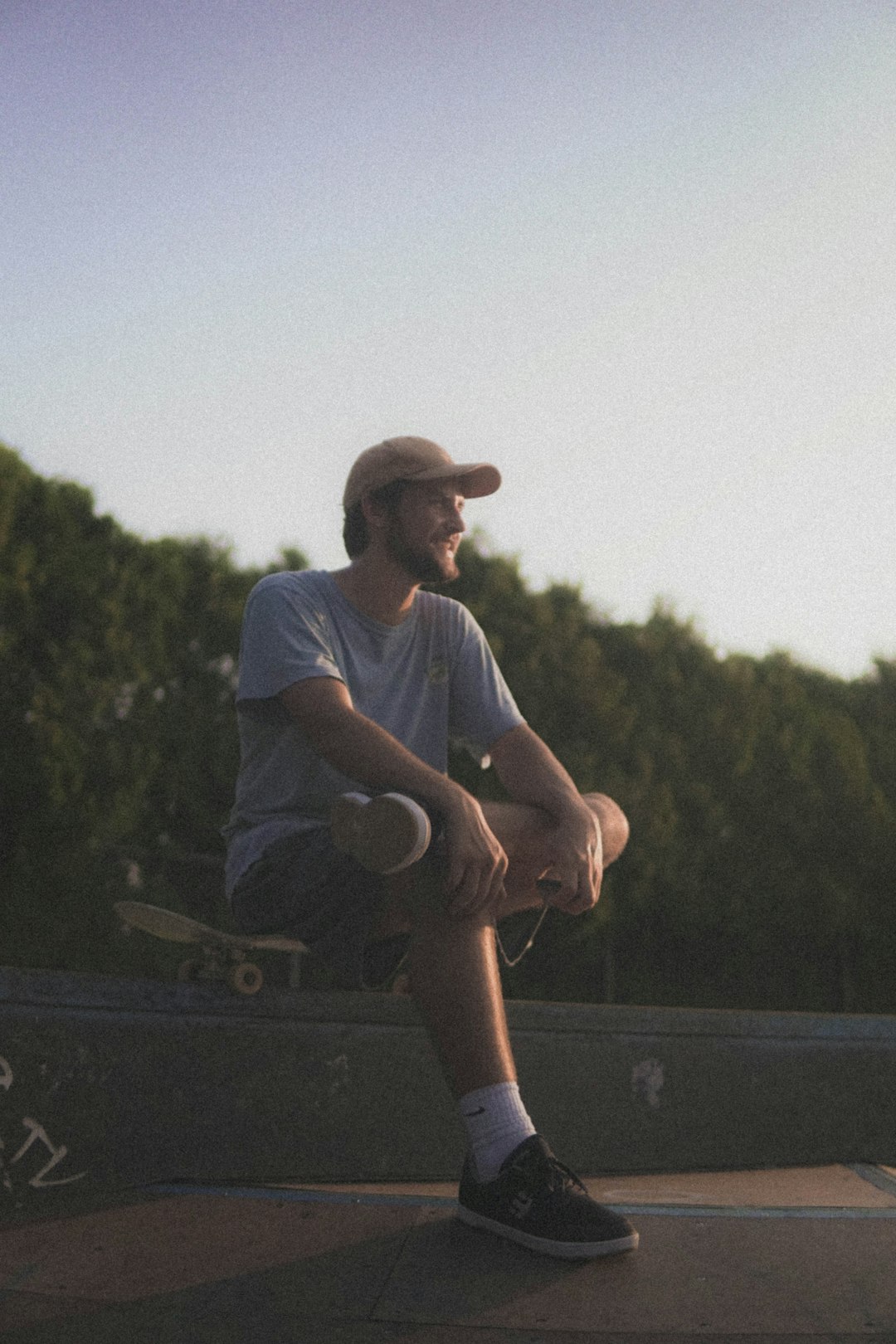 man in white crew neck t-shirt and brown shorts sitting on brown wooden fence during