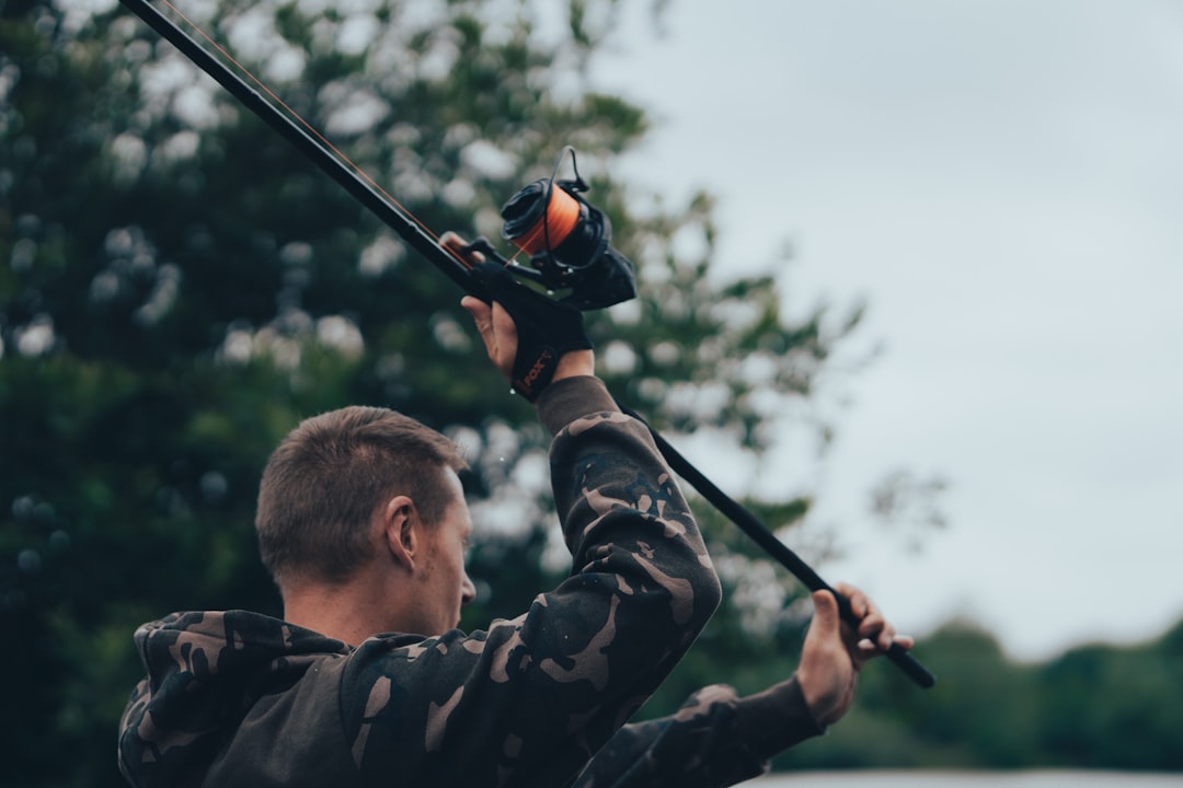 man in black and brown camouflage jacket holding black and red fishing rod