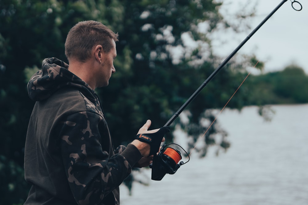 man in black jacket holding black and orange fishing rod