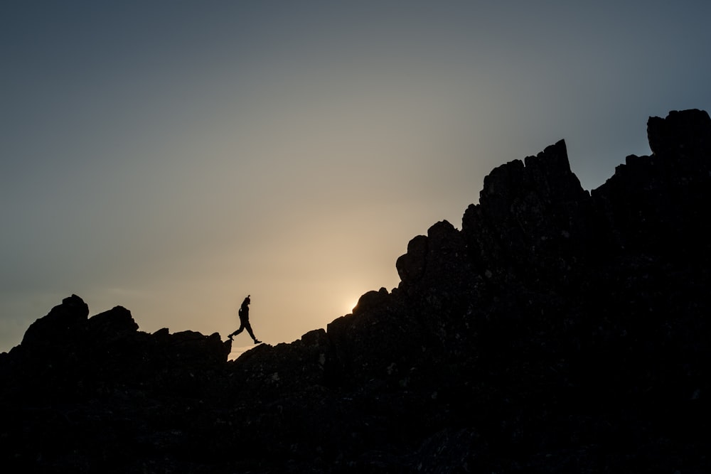 silhouette of person standing on rock formation during sunset