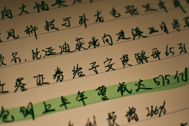 Several lines of handwritten Chinese characters are visible on a piece of paper, with one line highlighted in green. The text is written in dark ink, and the background is a light cream color.