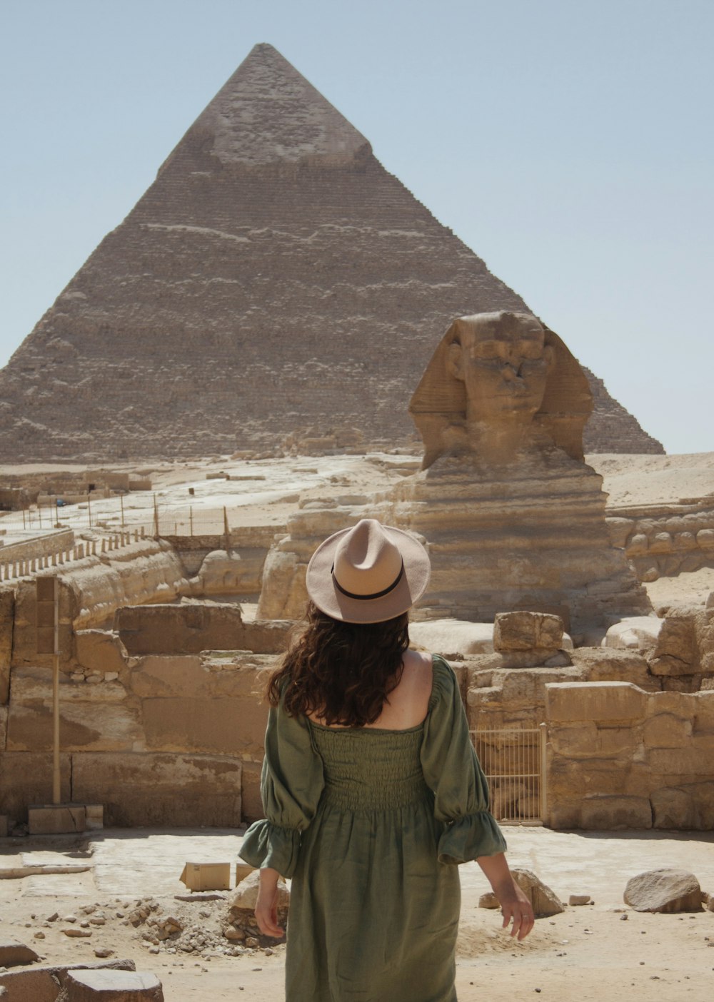 woman in green jacket wearing brown hat standing near pyramid during daytime