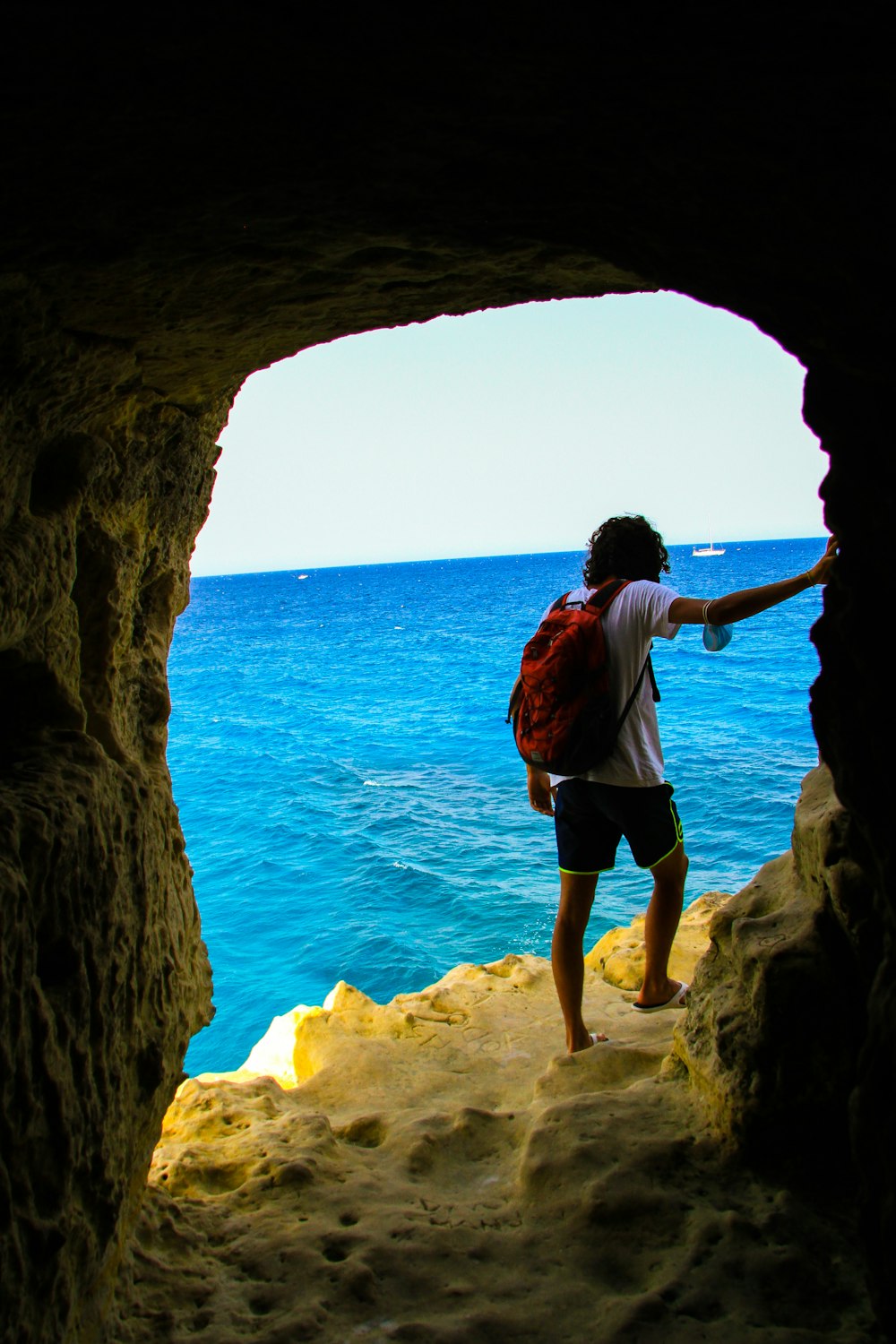 woman in white shirt and black shorts standing on brown rock formation near blue sea during