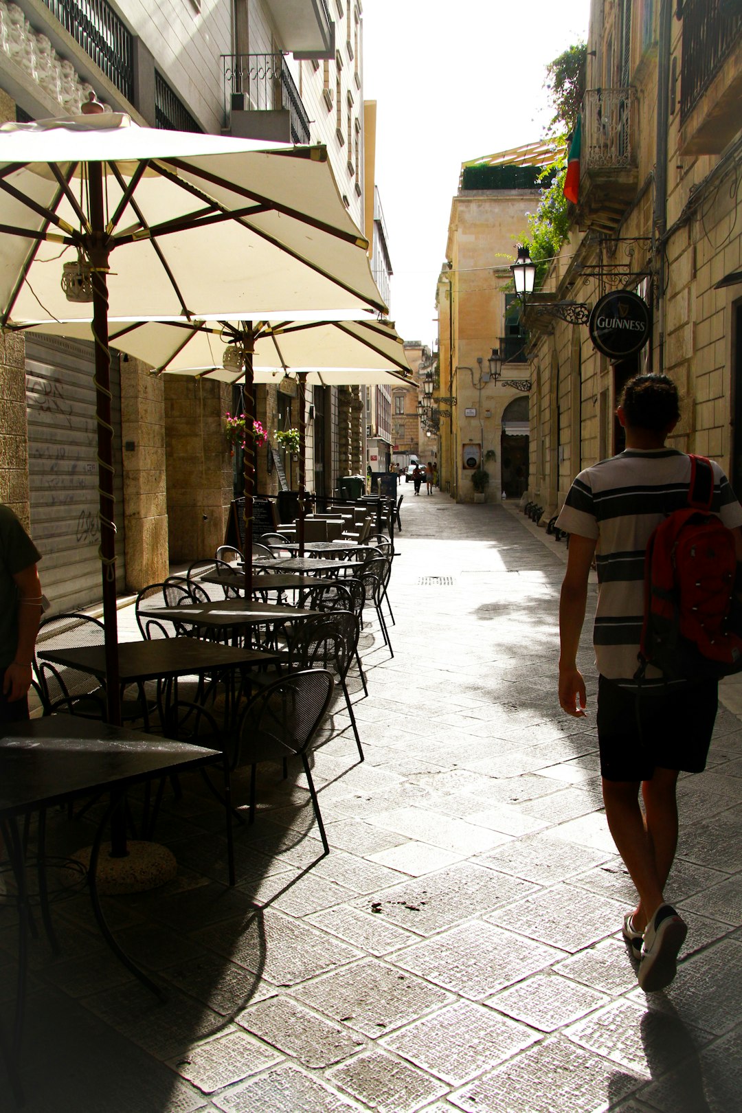 man in red and white stripe shirt walking on sidewalk during daytime