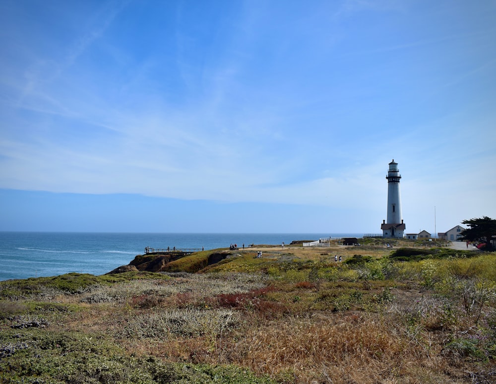 farol branco no campo de grama verde perto do corpo de água durante o dia