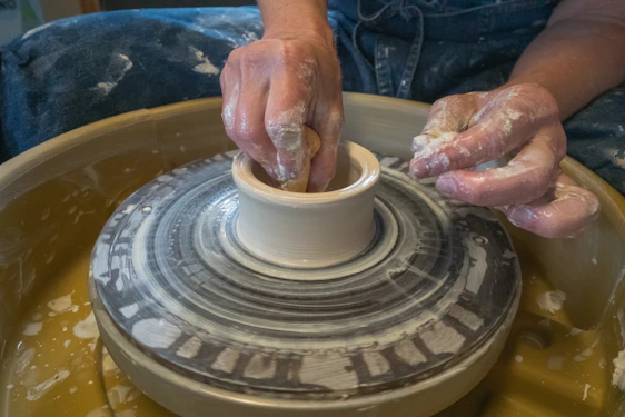 A cozy studio scene with hands shaping vibrant, hand-thrown stoneware on a potter’s wheel surrounded by colorful glazes.