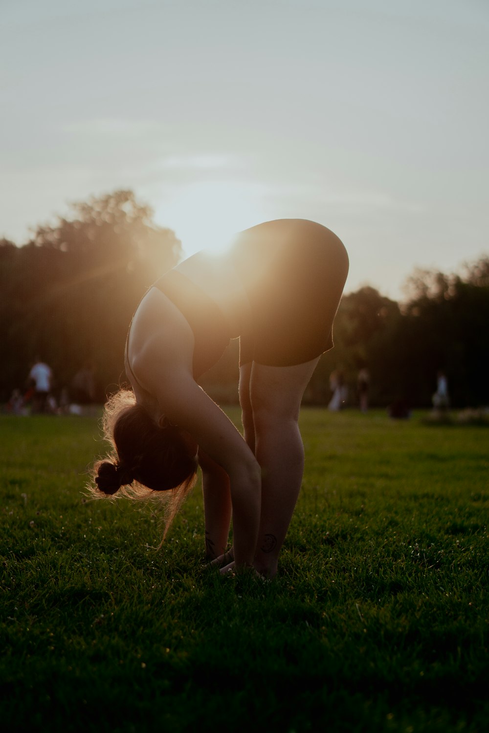 woman in white bikini bottom kneeling on green grass field during sunset