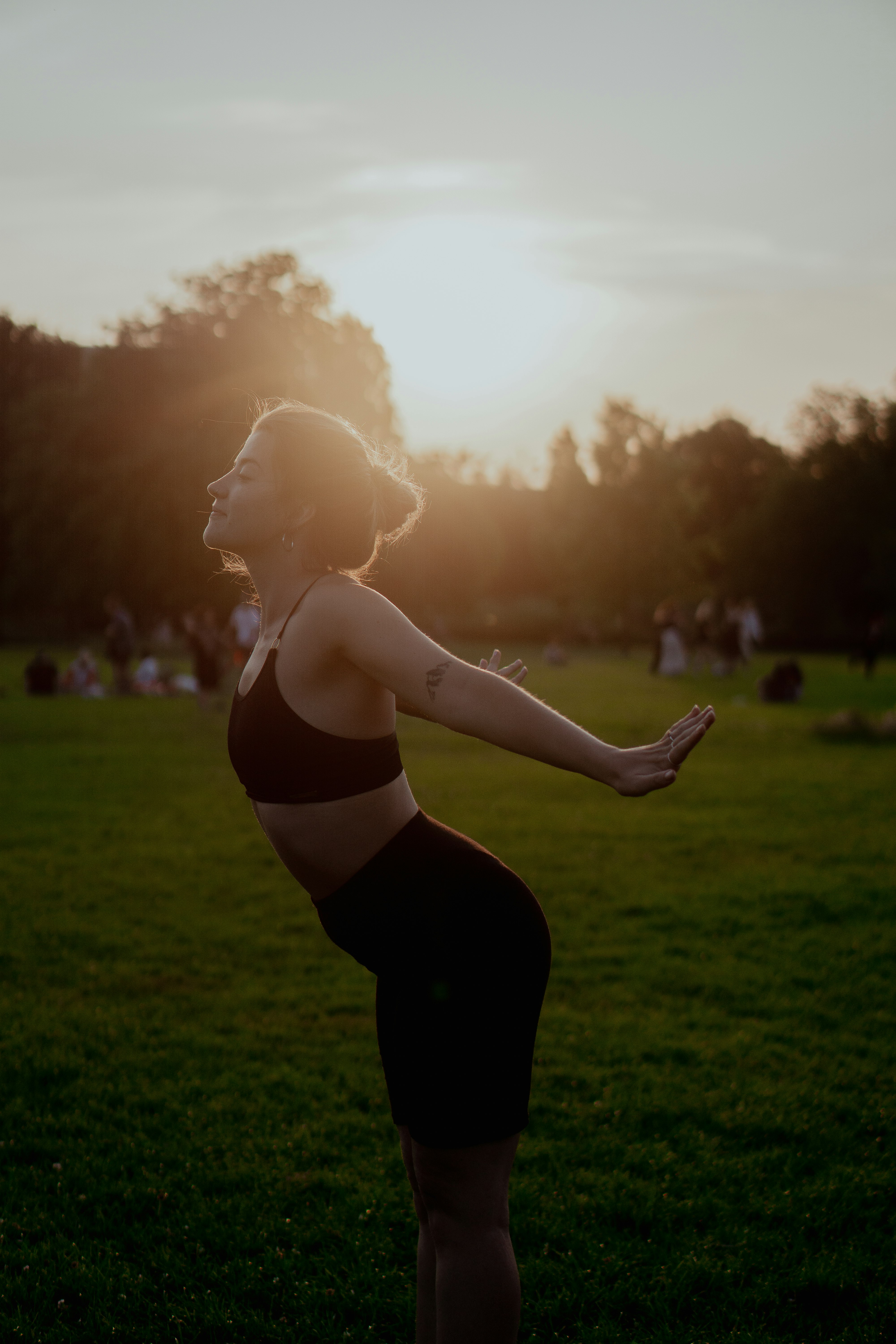 woman in black sports bra and leggings standing on green grass field during sunset