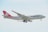 A large cargo airplane with the 'Cargolux' branding is captured mid-flight against a light, slightly cloudy sky. The aircraft has a predominantly white fuselage with a distinct red tail and engines. The branding and company logo are visible, along with the registration code on the side.