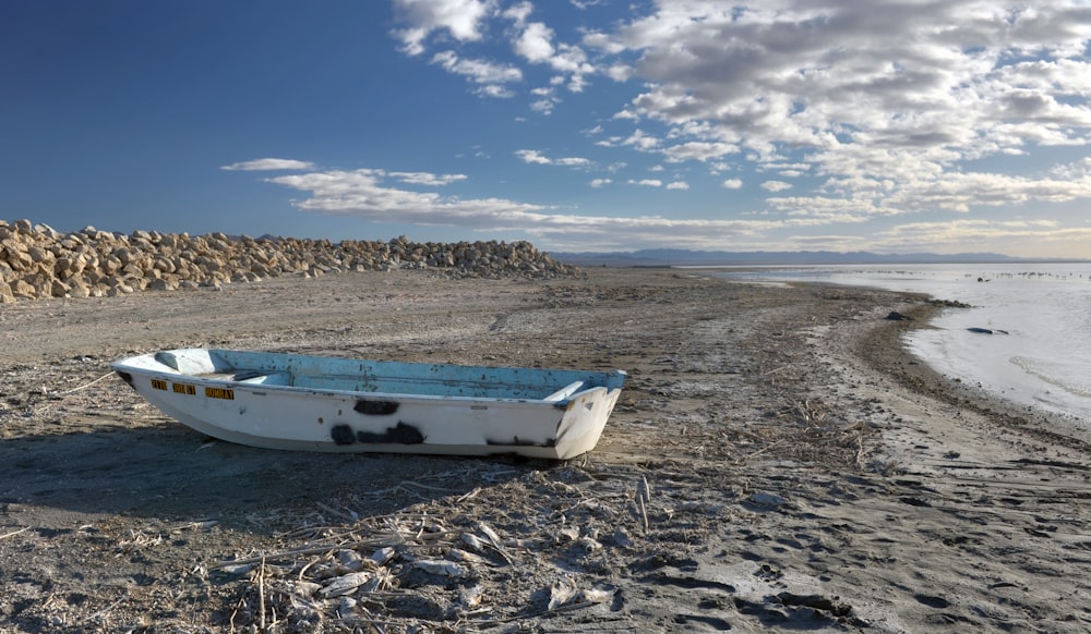 weißes und blaues Boot tagsüber auf braunem Sand unter blauem Himmel