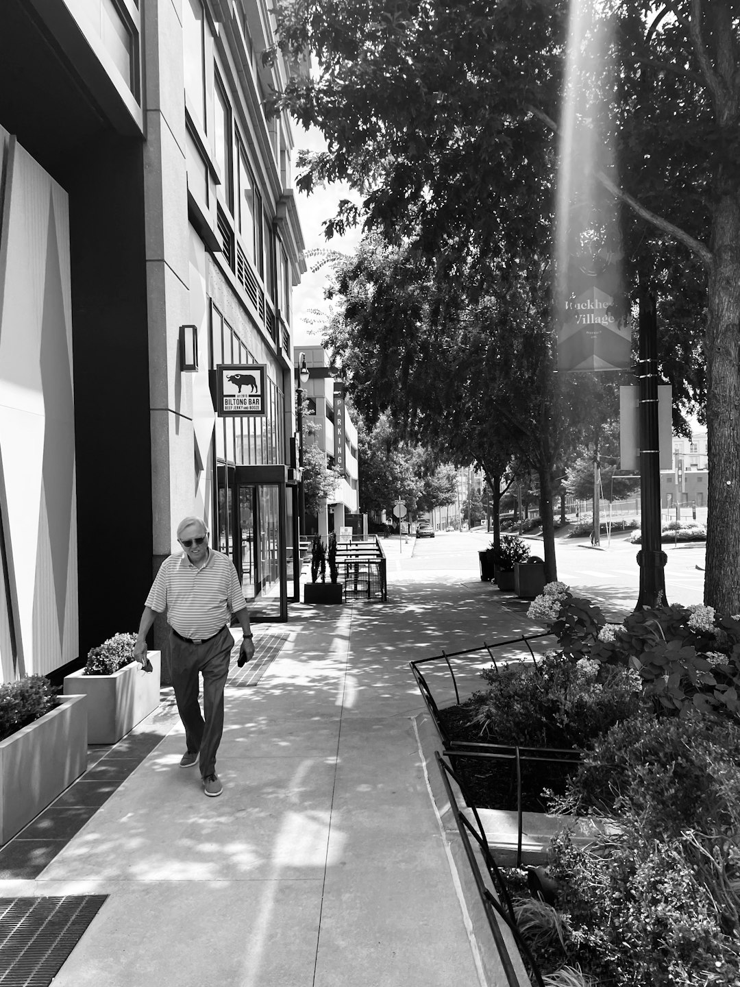 grayscale photo of man in white shirt and black pants walking on sidewalk