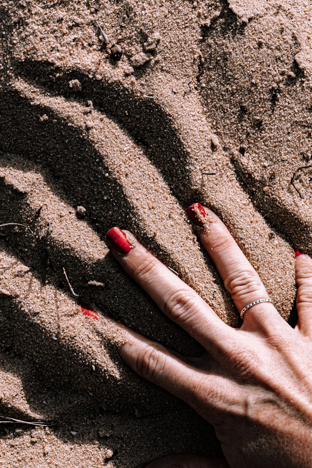 person with red manicure on brown sand