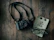 A black camera with a strap lies on a rustic wooden surface alongside a pair of eyeglasses and a journal with the text 'life is better with friends.' Two decorative buttons or pins are attached to the journal.