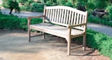 Wooden outdoor bench with natural grain, placed in a sunny garden setting.