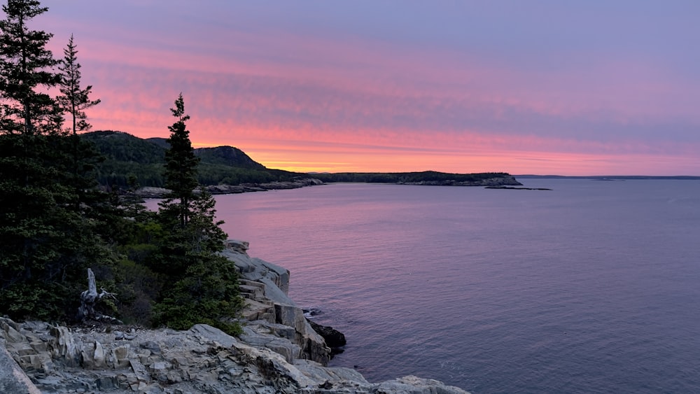 green trees on gray rocky mountain beside body of water during sunset