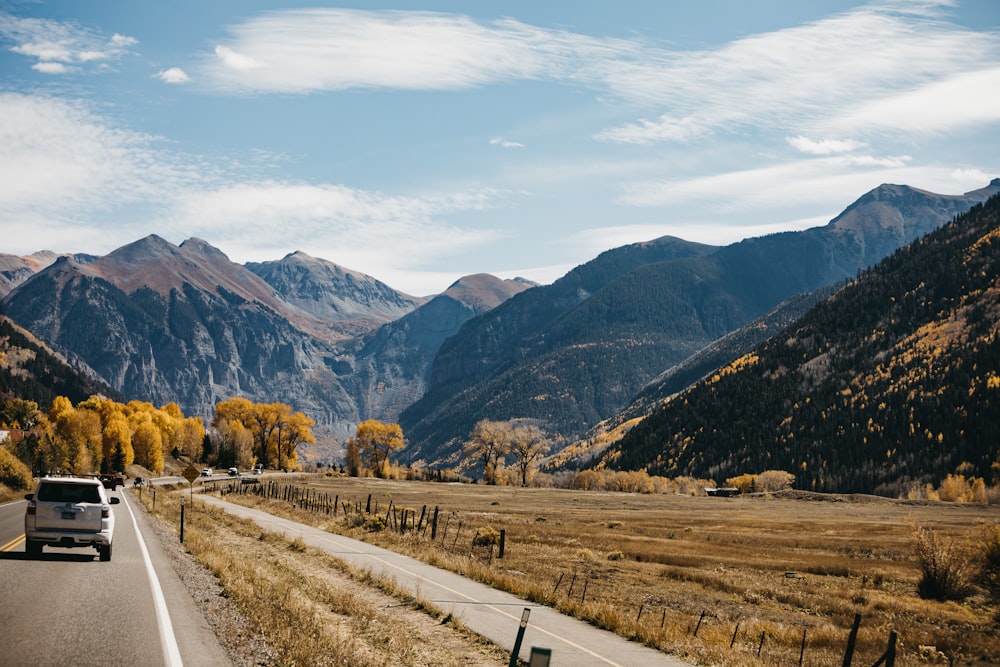 gray asphalt road between green grass field and mountains during daytime