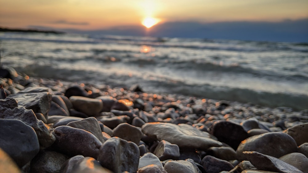 gray and white stones near body of water during sunset