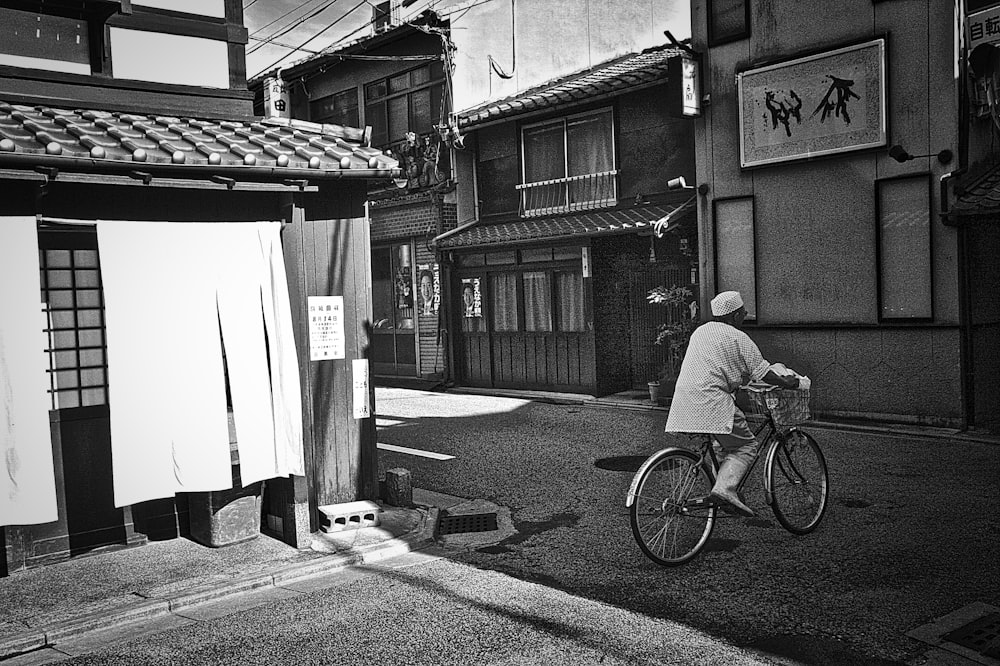 grayscale photo of man riding bicycle on road