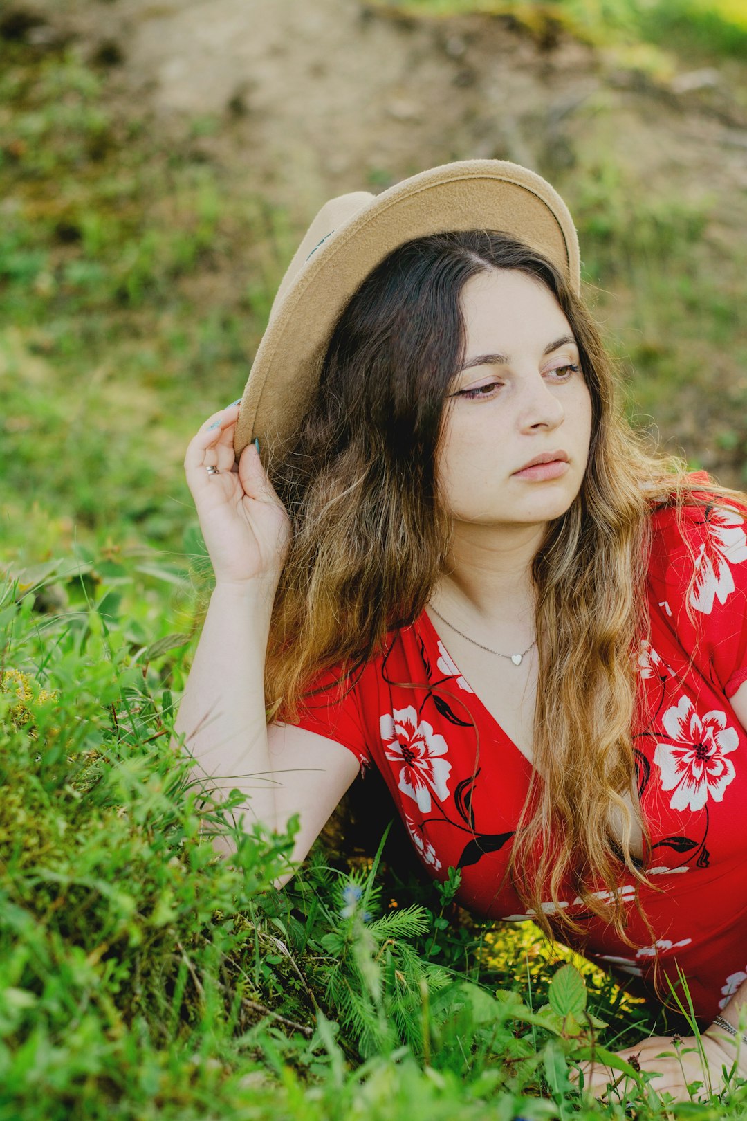 woman in red and white floral shirt wearing brown hat lying on green grass during daytime