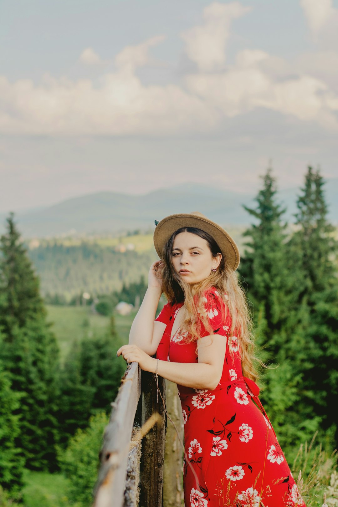 woman in red and white floral sleeveless dress wearing brown hat standing on green grass field