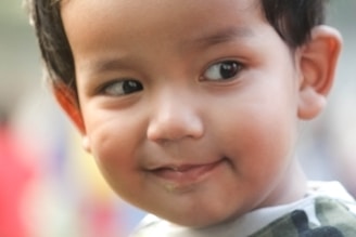 A young child with a gentle expression on their face. The soft focus and warm colors create a serene atmosphere. The child appears to be wearing a patterned shirt, and their hair is neatly combed.