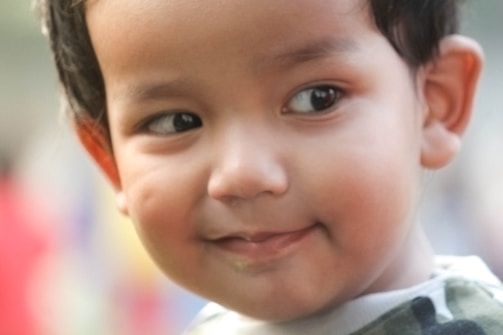 A young child with a gentle expression on their face. The soft focus and warm colors create a serene atmosphere. The child appears to be wearing a patterned shirt, and their hair is neatly combed.