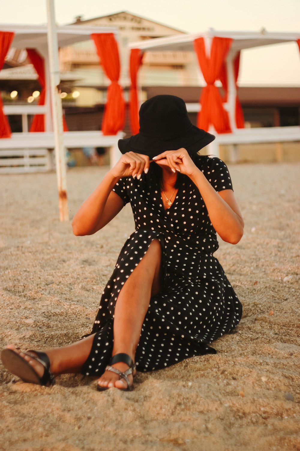 woman in black and white polka dot dress sitting on brown sand during daytime