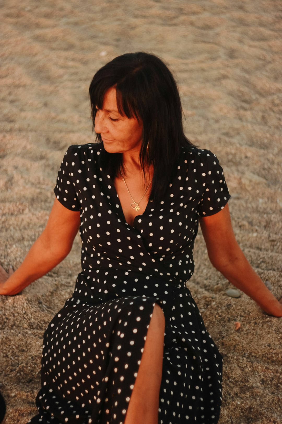 woman in black and white polka dot dress sitting on brown sand during daytime