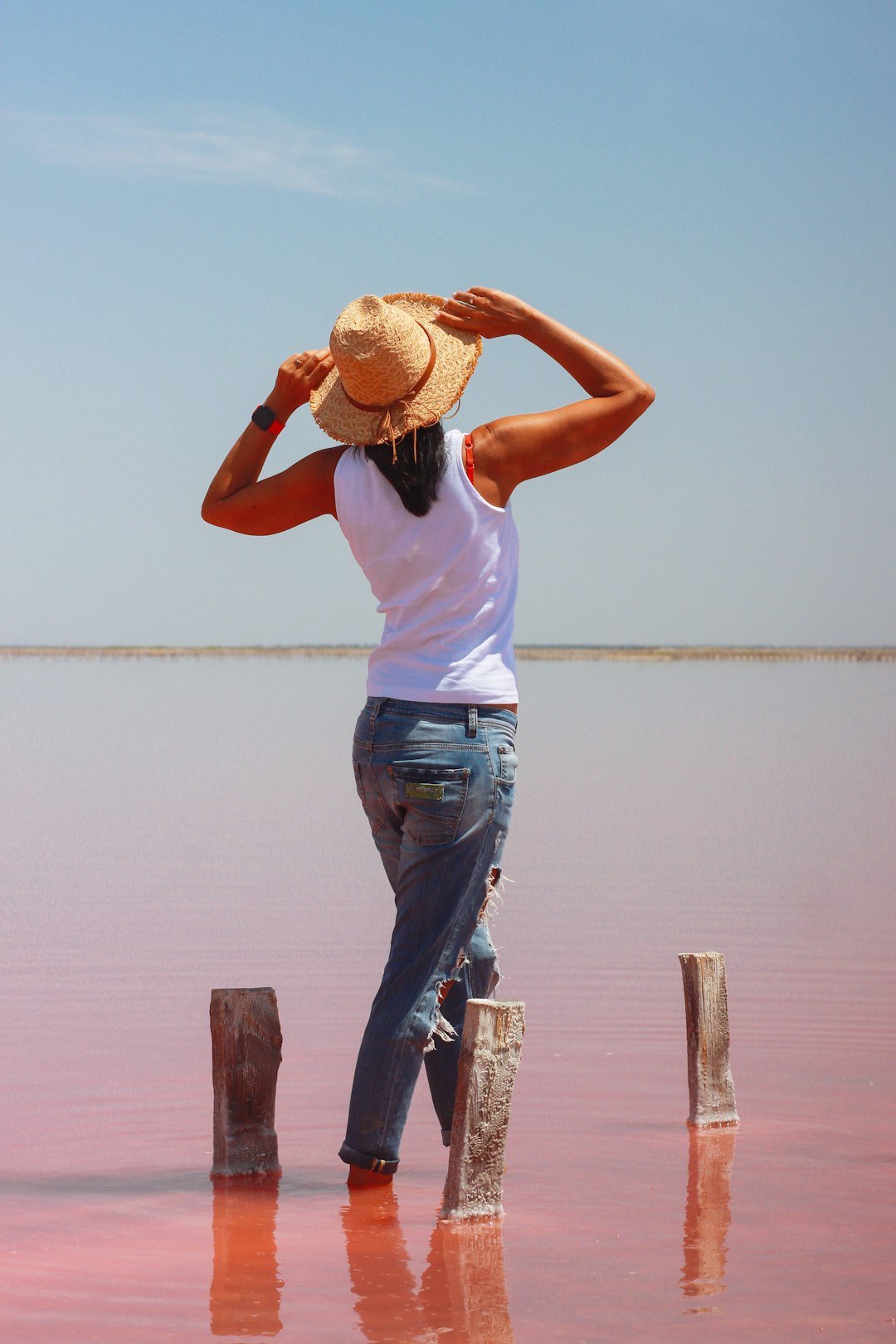 woman in white tank top and blue denim jeans standing on brown wooden dock during daytime