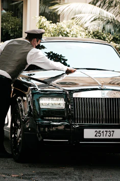 A friendly valet professional smiling while cleaning a sleek car outside a modern home.