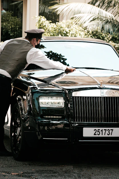 A professional technician carefully polishing a sleek car parked outside a modern apartment building.