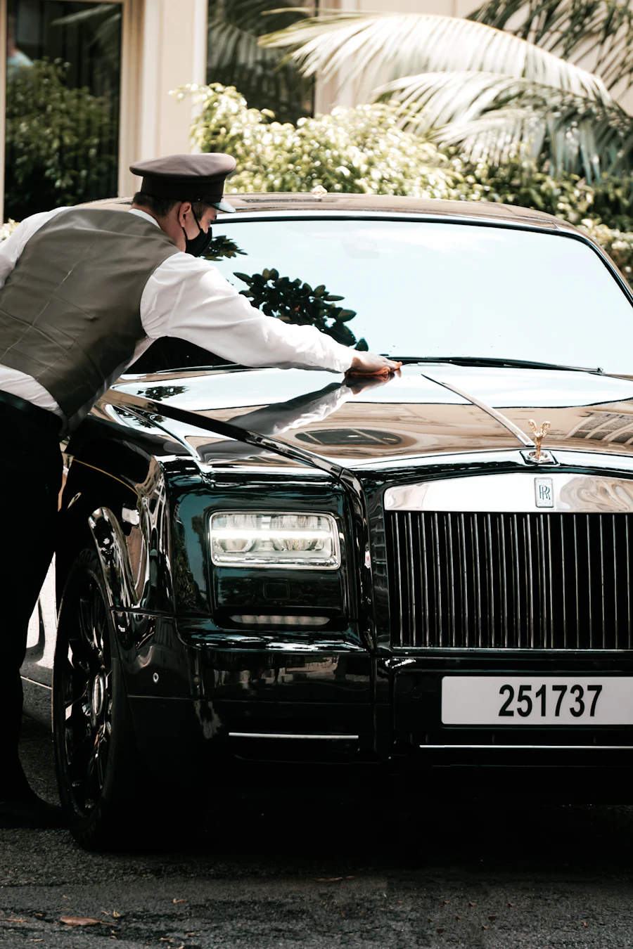 Chauffeur in a white shirt and cap standing beside a black car, waiting for a client