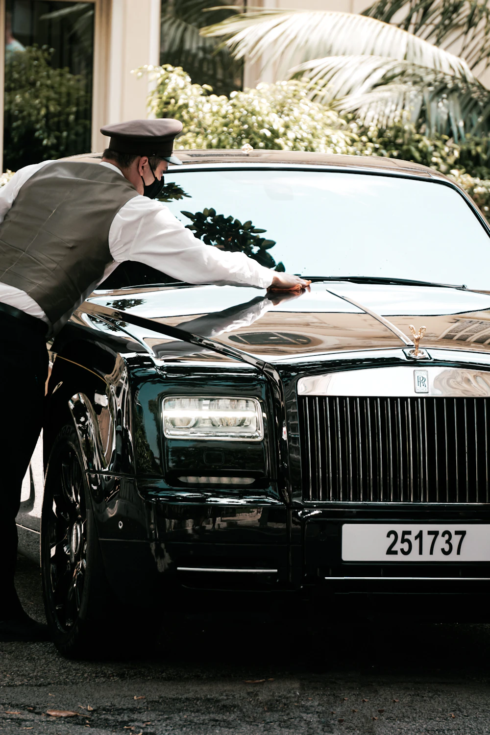 A uniformed chauffeur polishing a black Rolls-Royce