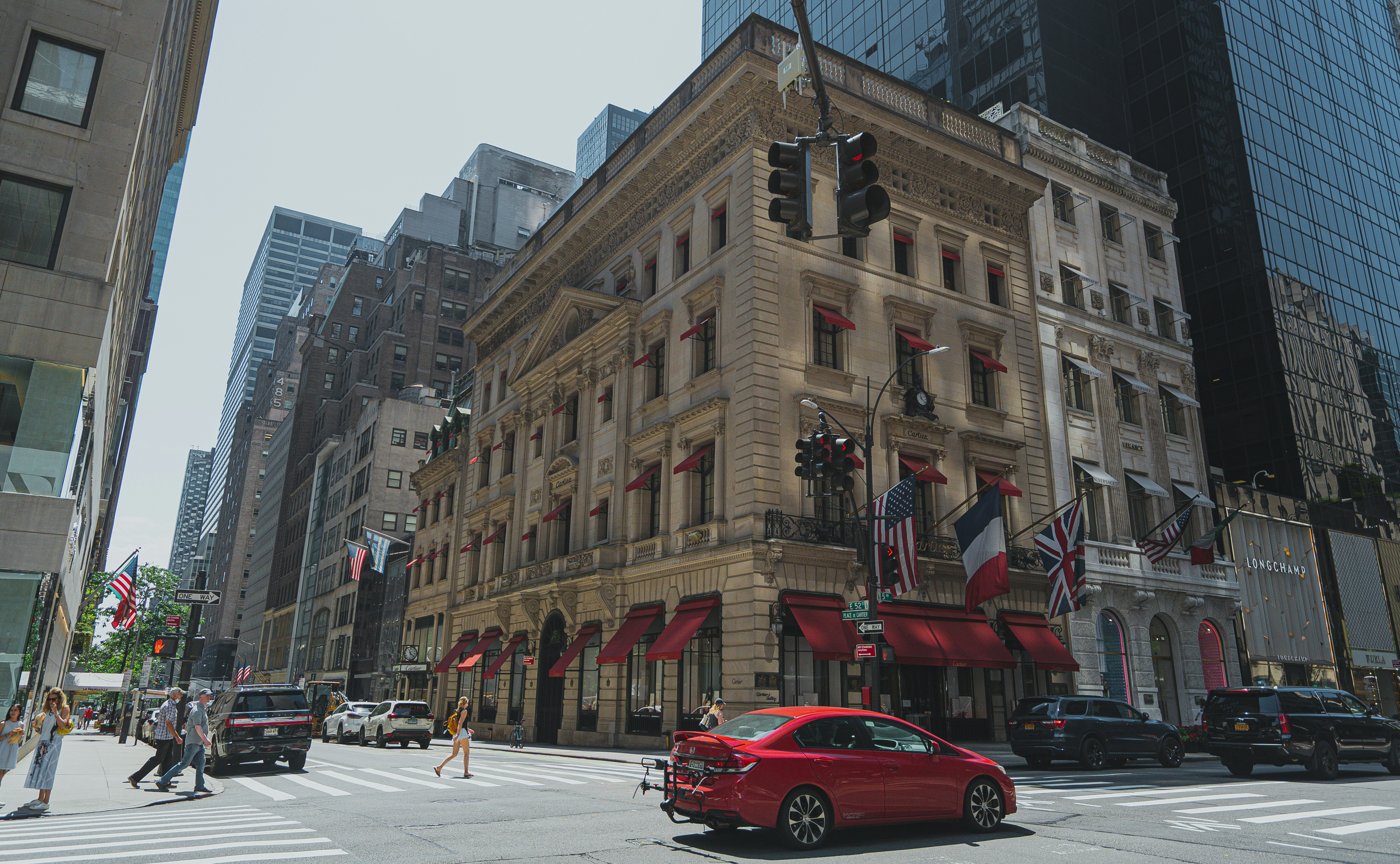 昼間、茶色のコンクリートの建物近くの道路を走る赤いセダン