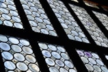 A set of round paneled windows featuring a pattern of circular glass pieces arranged in a grid. The glass has varying levels of transparency, with some displaying a slight iridescent effect. The framework is dark, contrasting with the light filtering through the windows.