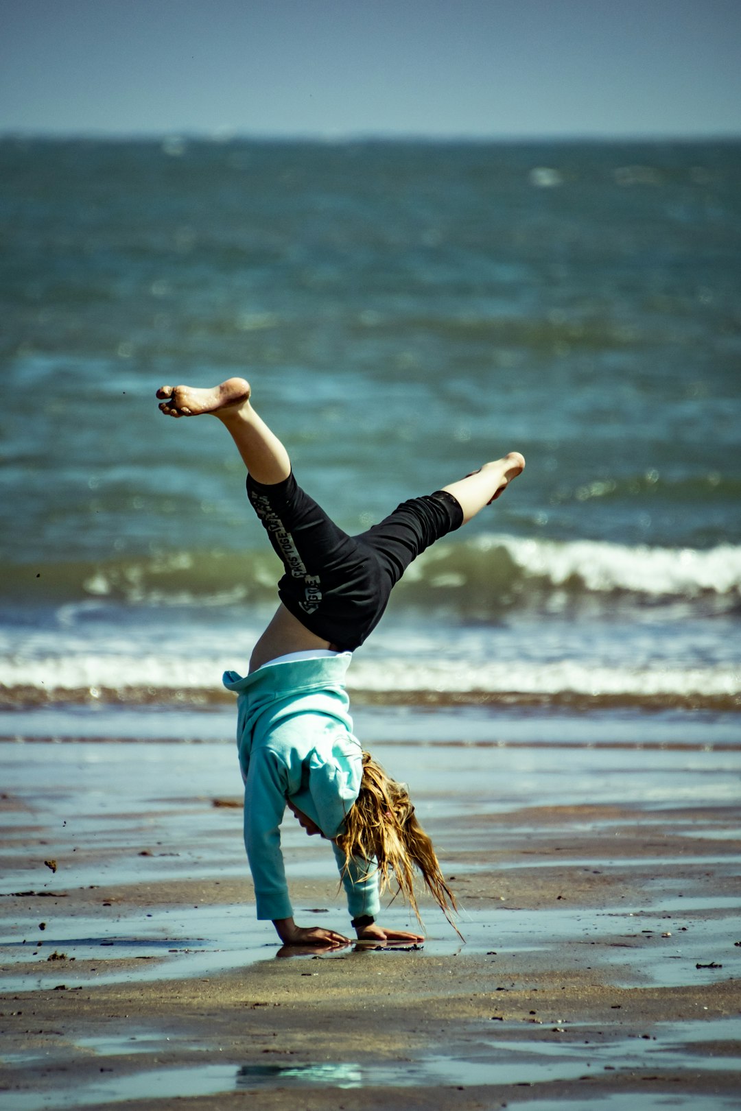 woman in black long sleeve shirt and blue denim shorts jumping on beach during daytime