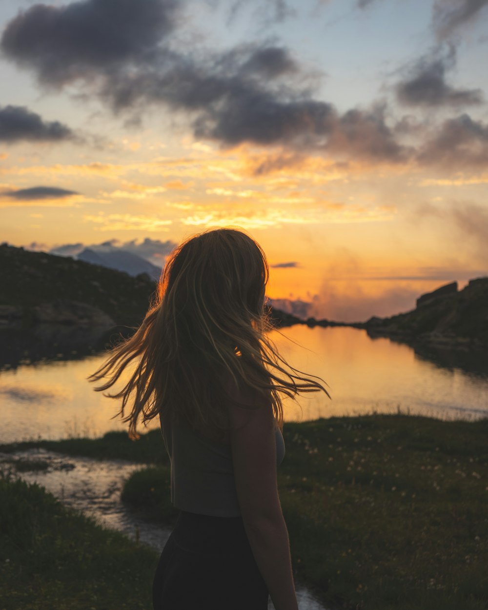 woman in white long sleeve shirt standing on green grass field during sunset