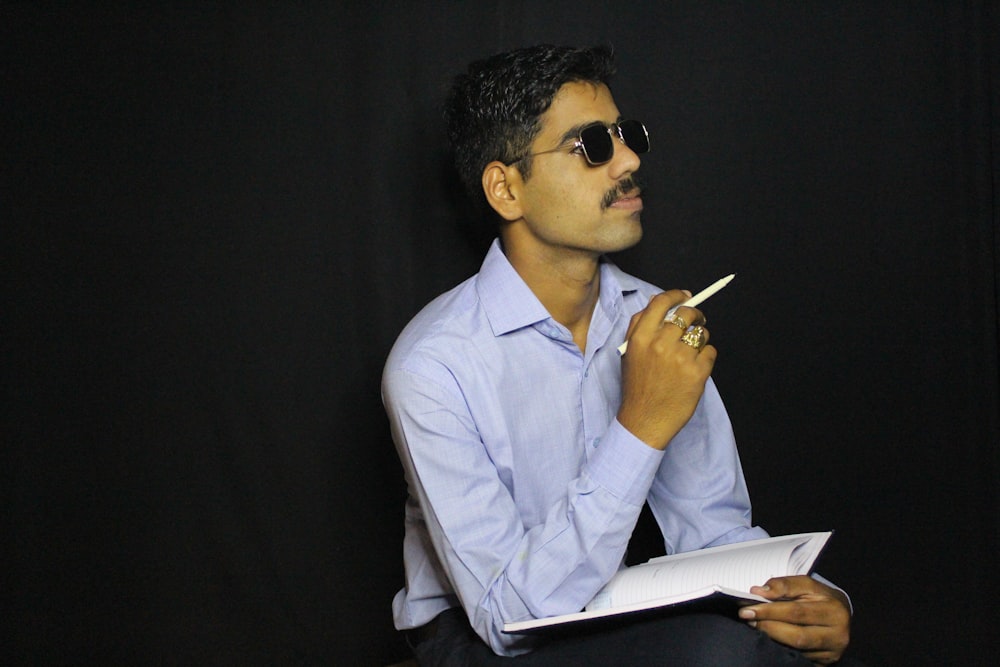 man in white dress shirt wearing black sunglasses holding pen