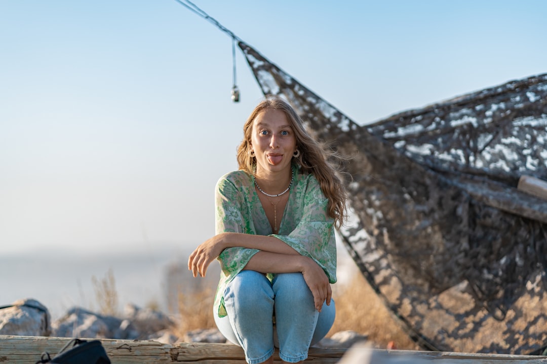 woman in green long sleeve shirt and blue denim jeans sitting on brown rock during daytime