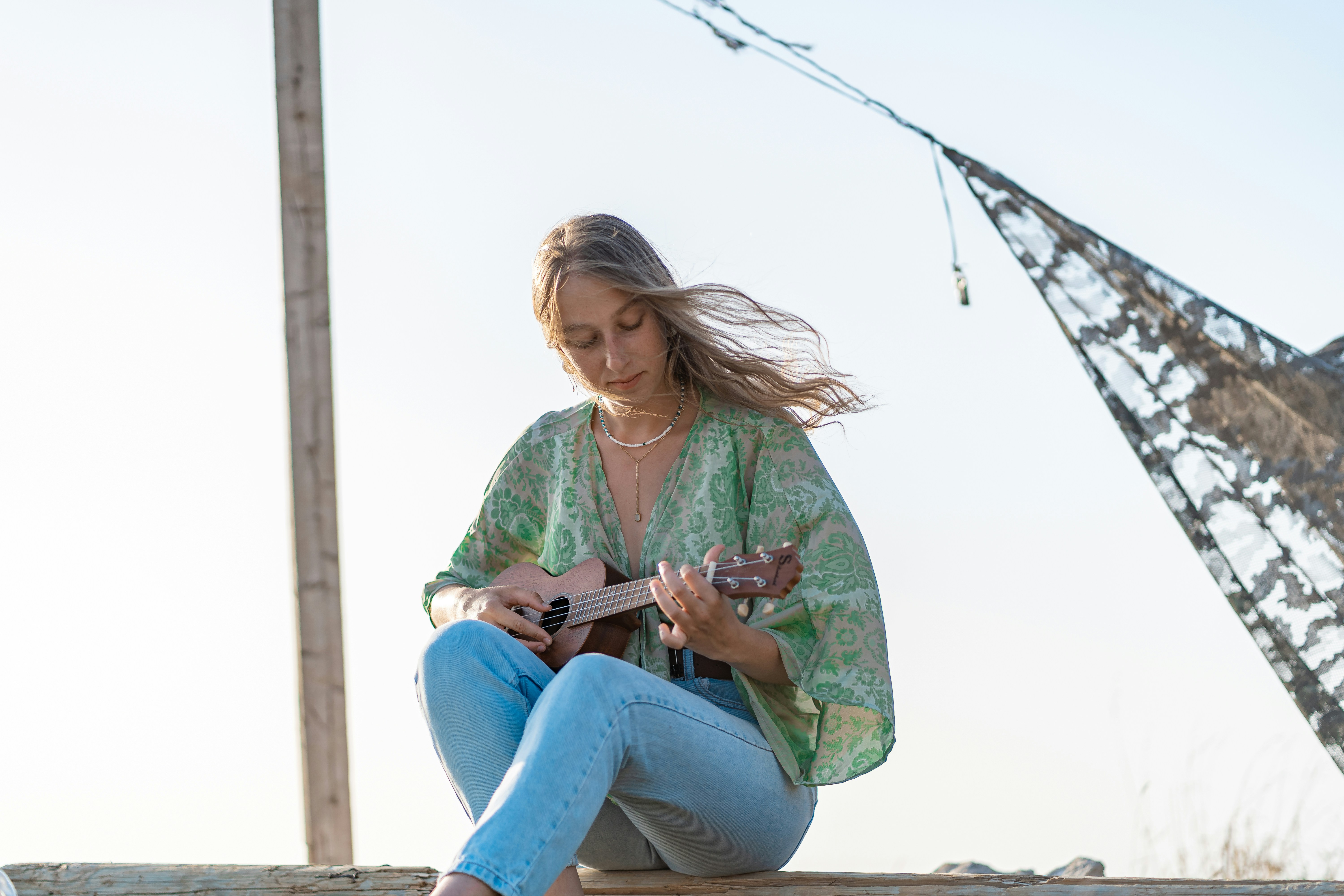 woman in green long sleeve shirt and blue denim jeans sitting on white wooden post during