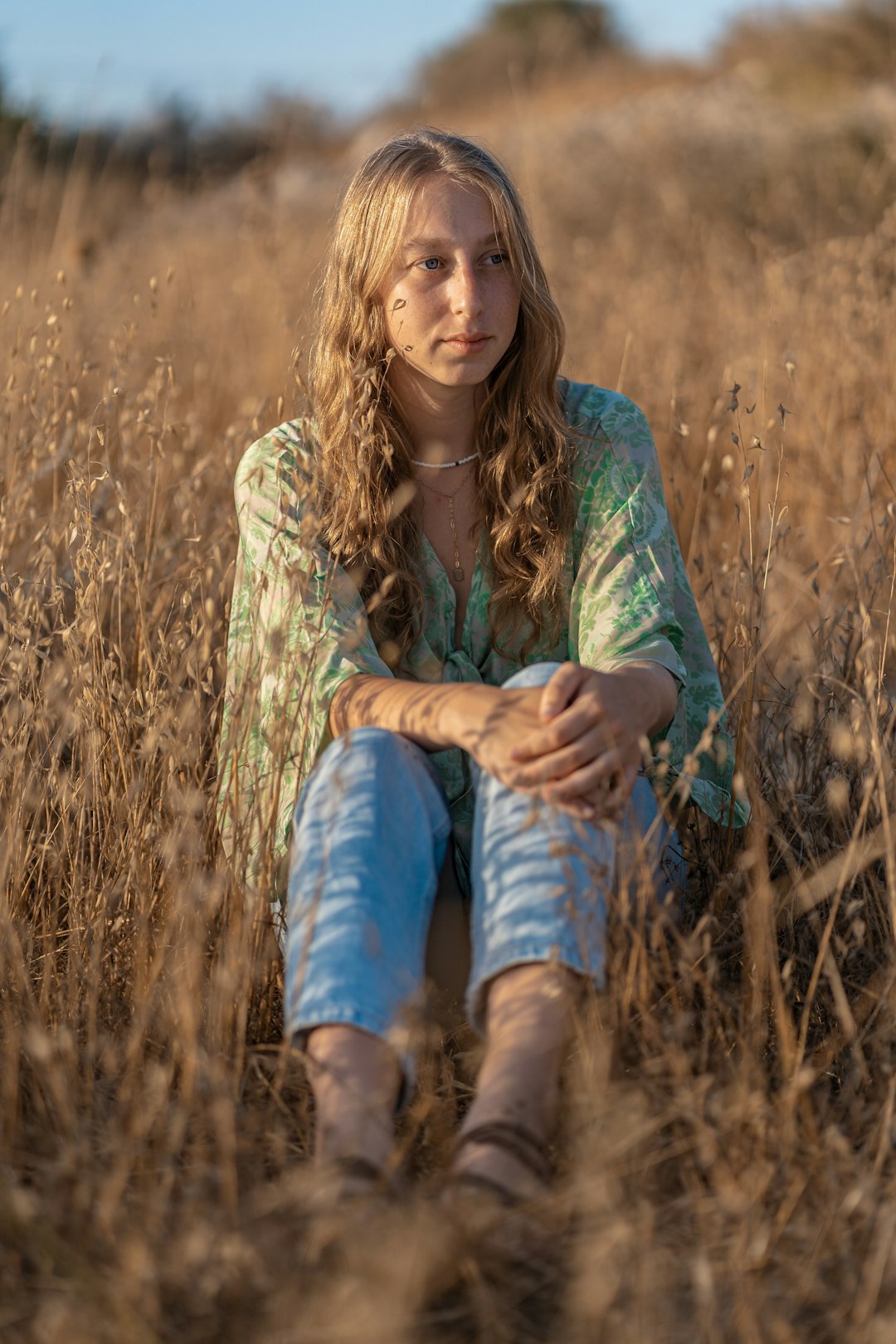 woman in green long sleeve shirt and blue denim jeans sitting on brown grass field during