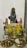 A religious altar setup featuring a blue deity statue adorned with a pearl necklace and a crown. Two smaller gold statues flank the main idol, and they are surrounded by offerings such as bananas, a mango, and a lime. There's a decoration of yellow flowers, and traditional brass utensils including lamps and a bowl with grains and coins.