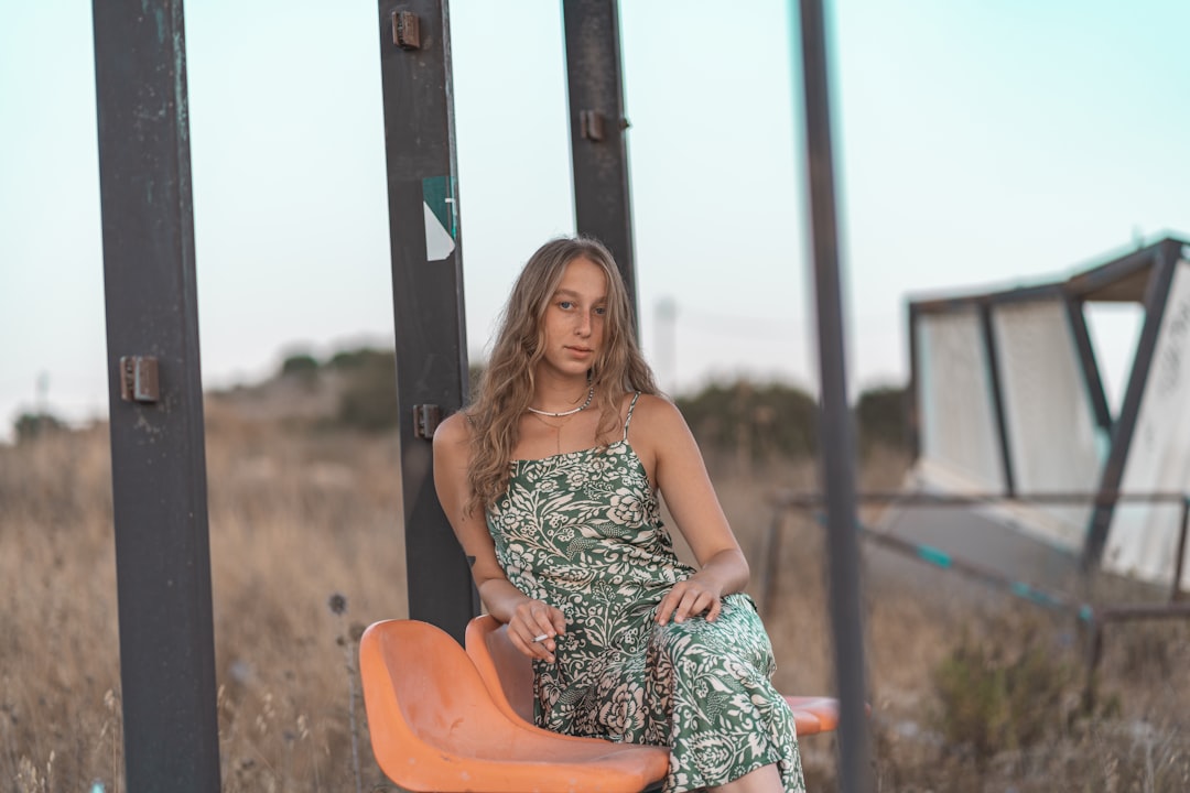 woman in green and white floral spaghetti strap dress sitting on orange chair