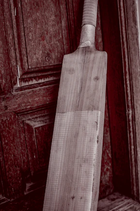Close-up of a worn cricket bat being expertly repaired with tools on a wooden workbench.
